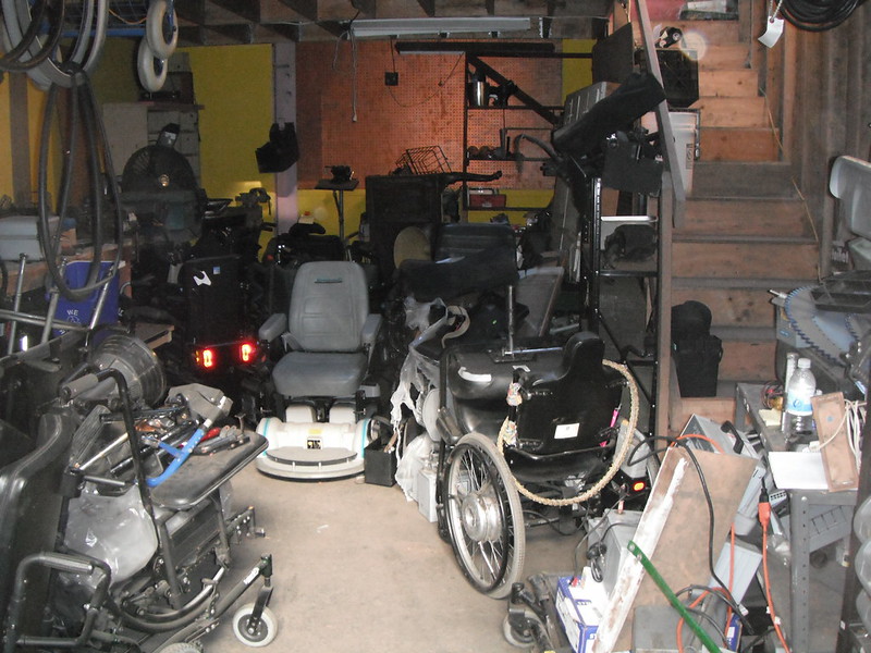 a jumble of wheelchairs and wheelchair parts in a workshop