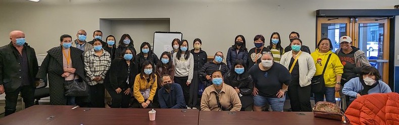 a row of masked people in a conference room posing for a group pic