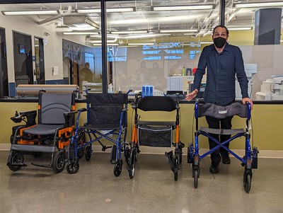 a man posing next to a row of loaner rollators, manual wheelchairs, and powerchairs