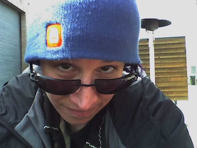 younger liz peering over sunglasses wearing a beanie hat with the blue, white, and orange Blogger logo 