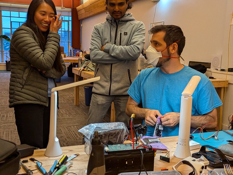 three people gathered around an electronics workbench