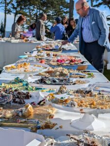 a long table covered in the remains of many many different cakes. a man leans over and puts a finger into one in the distance