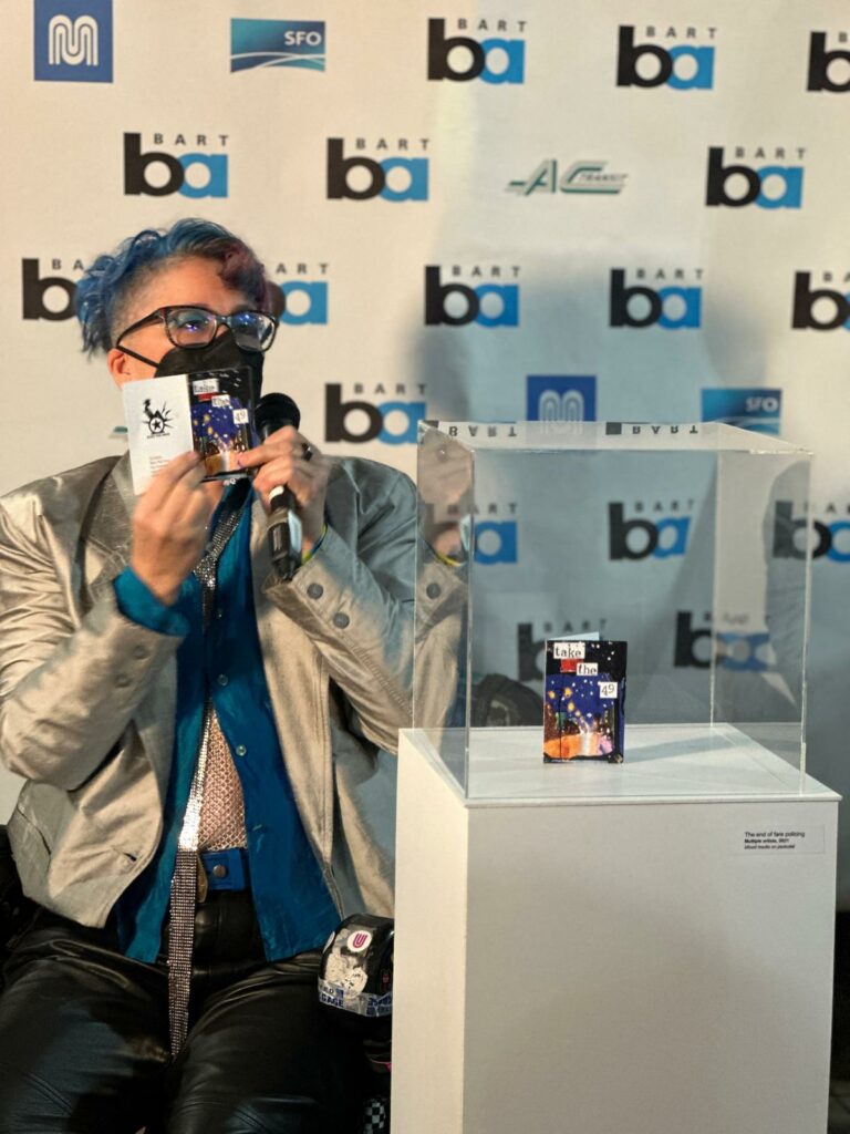 liz holding up a tiny zine; another copy is in a glass case beside them