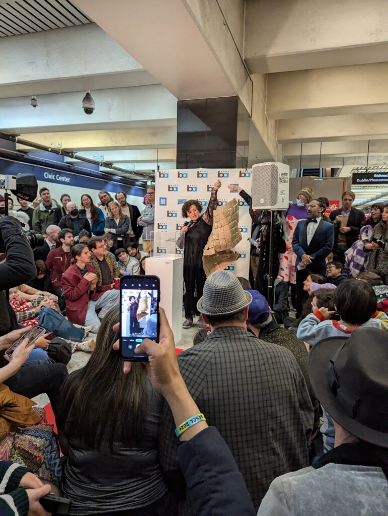 a lady holding up a woven sculpture in a huge crowd in the train station