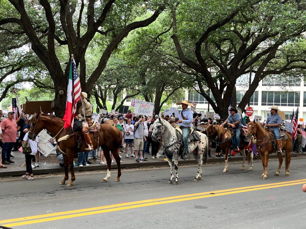 men on horseback in a no kings parade in texas, us and mexican flags flying