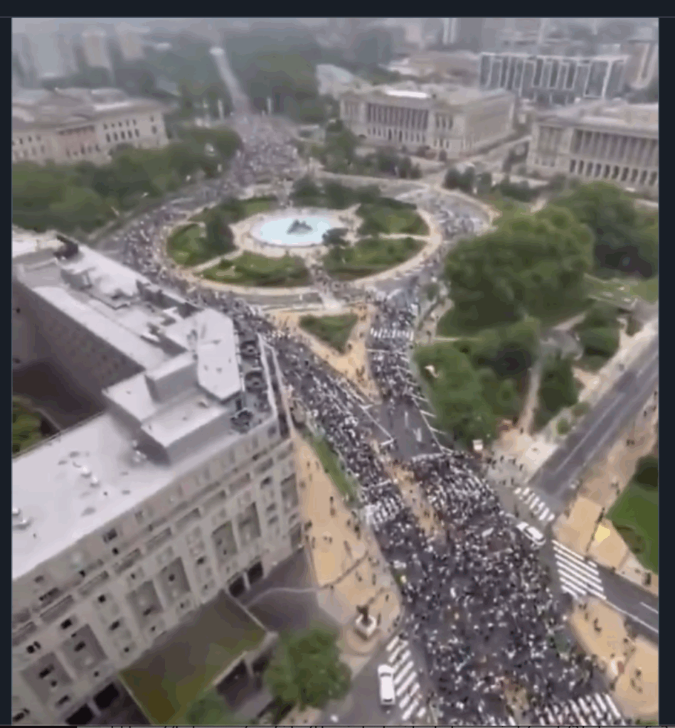 screenshot of a bit of aerial video of huge crowds filling several streets and plazas