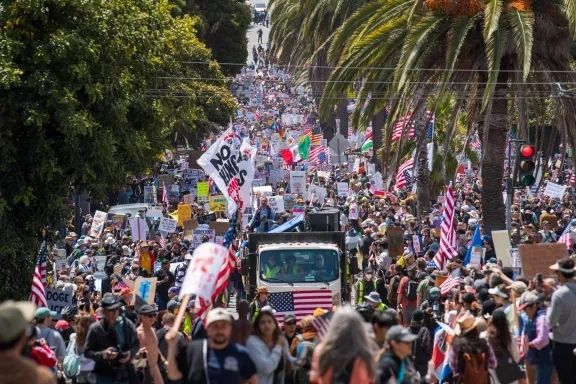 a large crowd streaming down palm tree lined Dolores St. in San Francisco, view over several city blocks