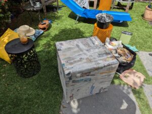 a box covered in wet newspaper on the grass surrounded by piles of supplies, flour and water