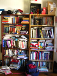 two large bookshelves in absolute chaos, stuffed with books double stacked and going every which way.