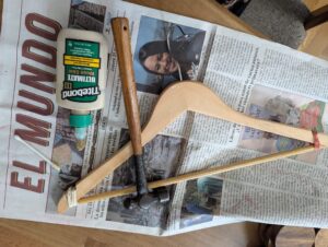 a wooden hanger with a hammer, glue, and rubber band clamps on a sheet of old newspaper